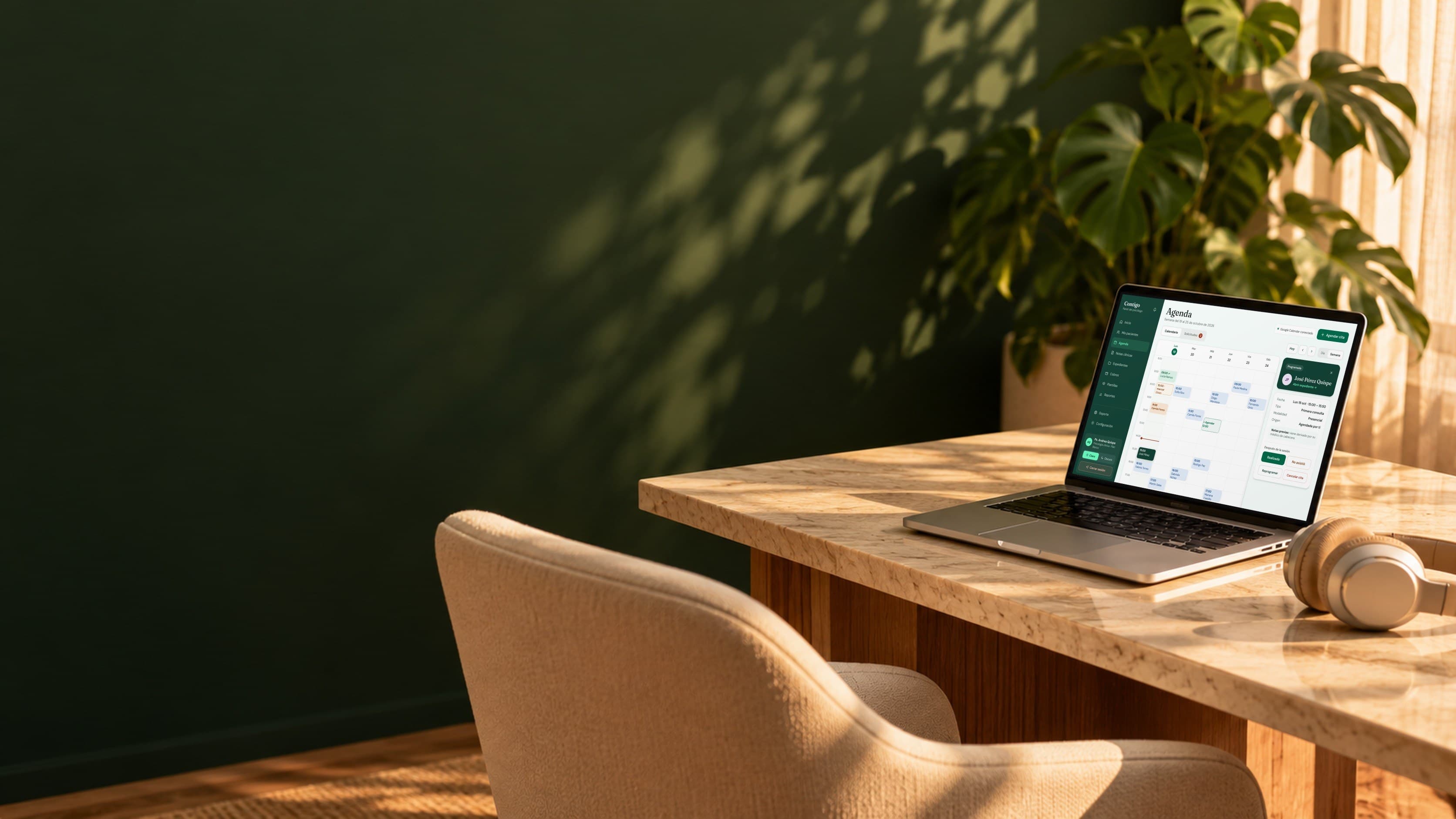 Laptop con la Agenda de Contigo sobre un escritorio de mármol junto a una silla y unos audífonos
